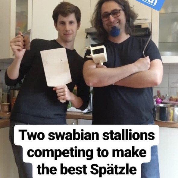 Ein ungleiches schwäbisches Herren-Duo wie in einer Buddy-Cop-Komödie steht in einer Küche mit Spätzlezubehör in der Hand und grinst in die Kamera. Unten steht 'Two swabian stallions competing to make the best Spätzle'